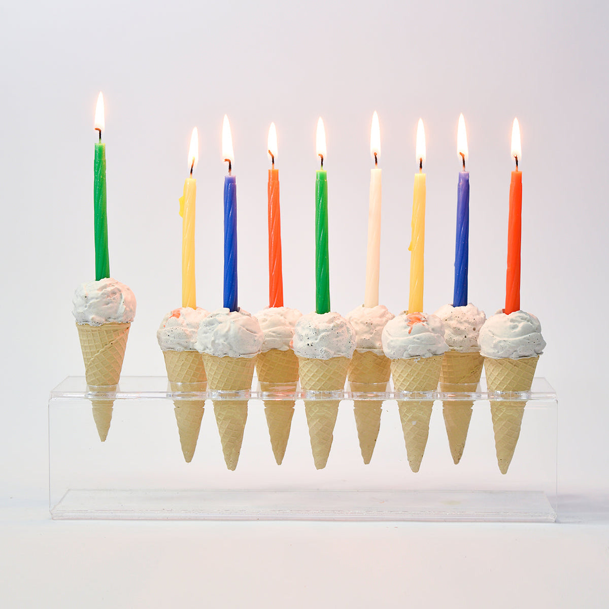 חנוכיית גלידה עם 9 נרות צבעוניים על מעמד אקריליק שקוף.